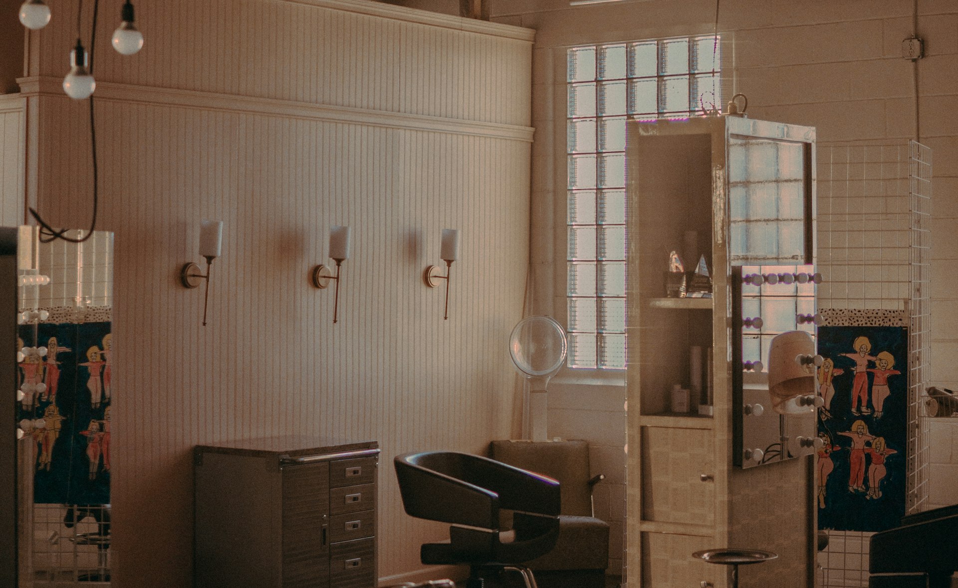A warm independent hair salon interior: wash basin, sconce lights and salon mirrors in soft evening light
